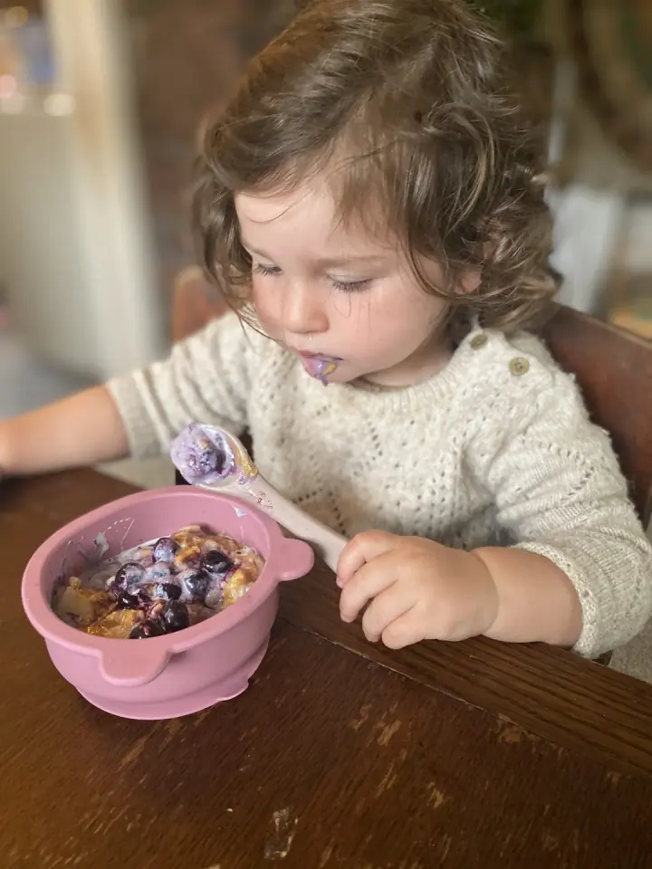 A toddler eating independently from a bowl.