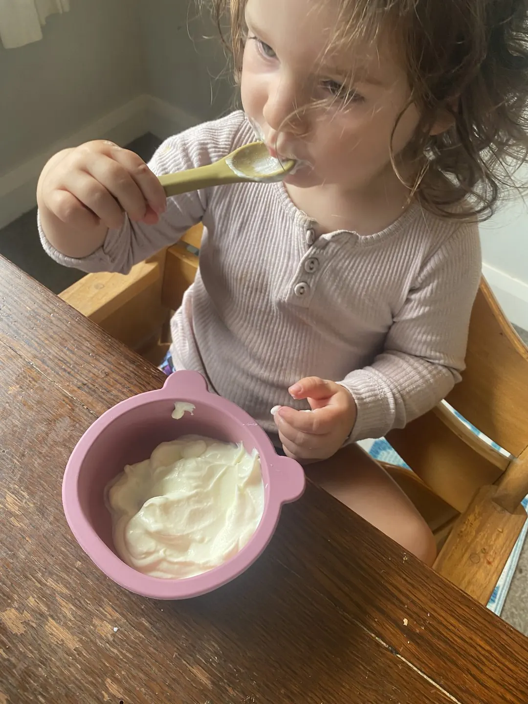 A toddler using a bowl and spoon at mealtime.