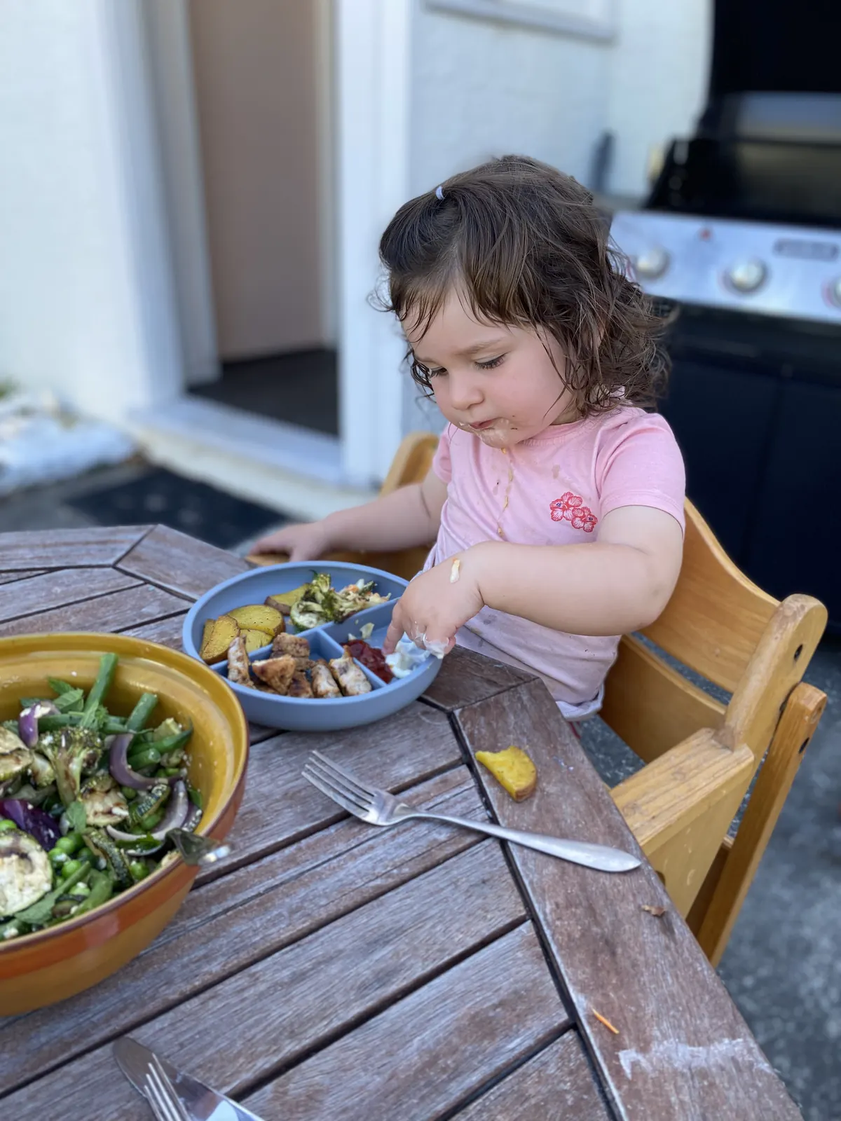 An older child using a blue divided plate outdoors.