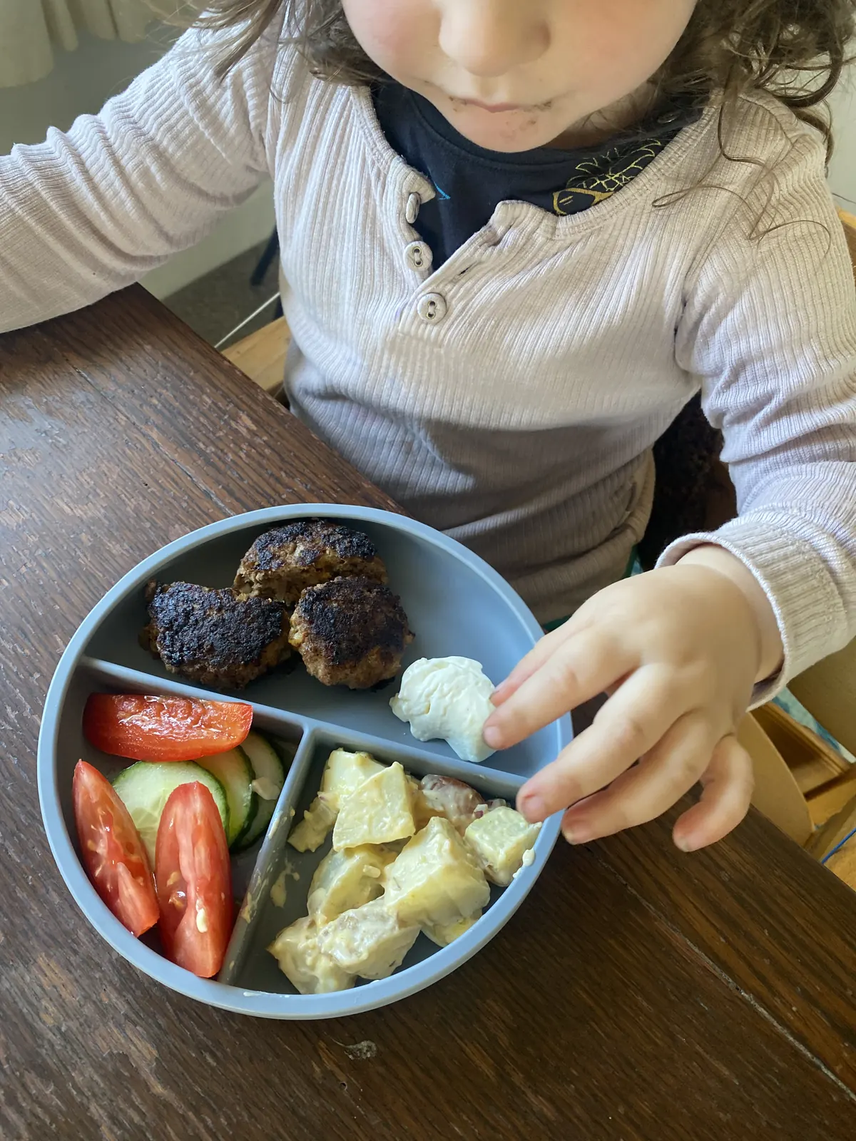 A child exploring a meal from a blue divided plate.