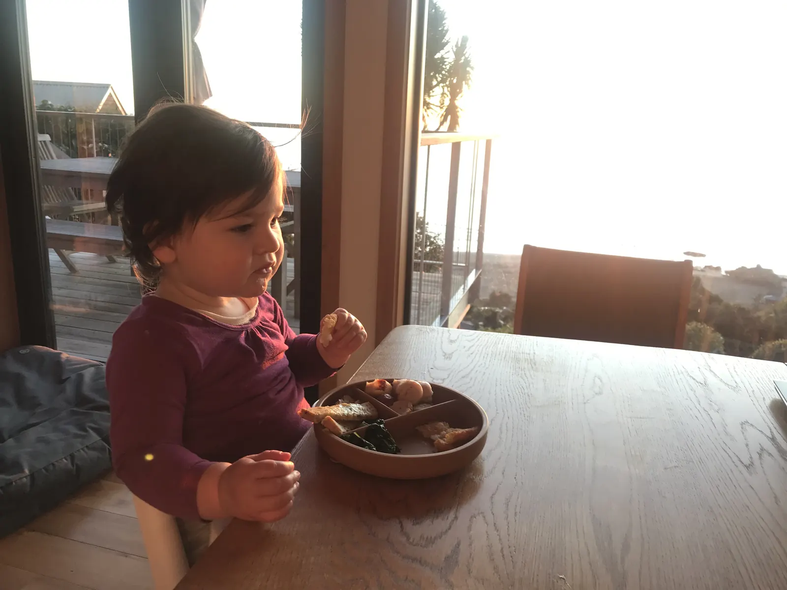 A toddler using an earthy divided plate indoors.
