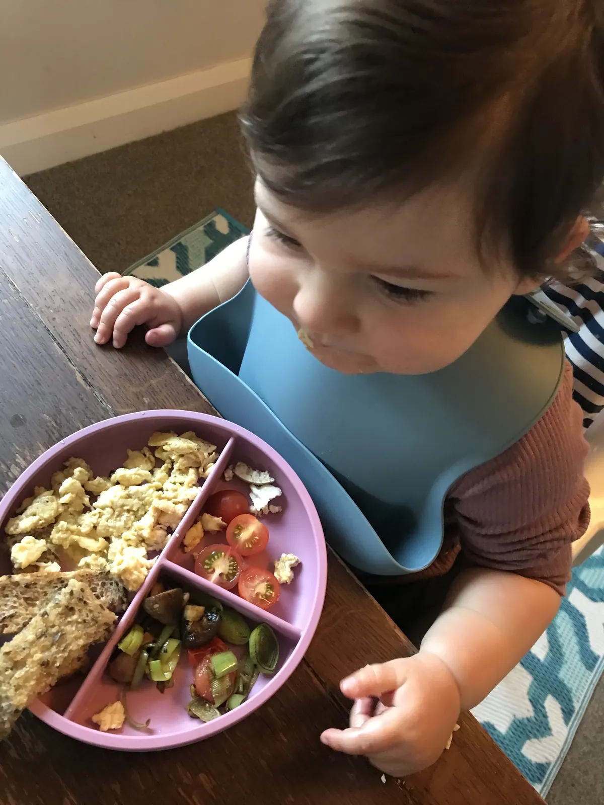A baby learning to self-feed from a pink divided plate.