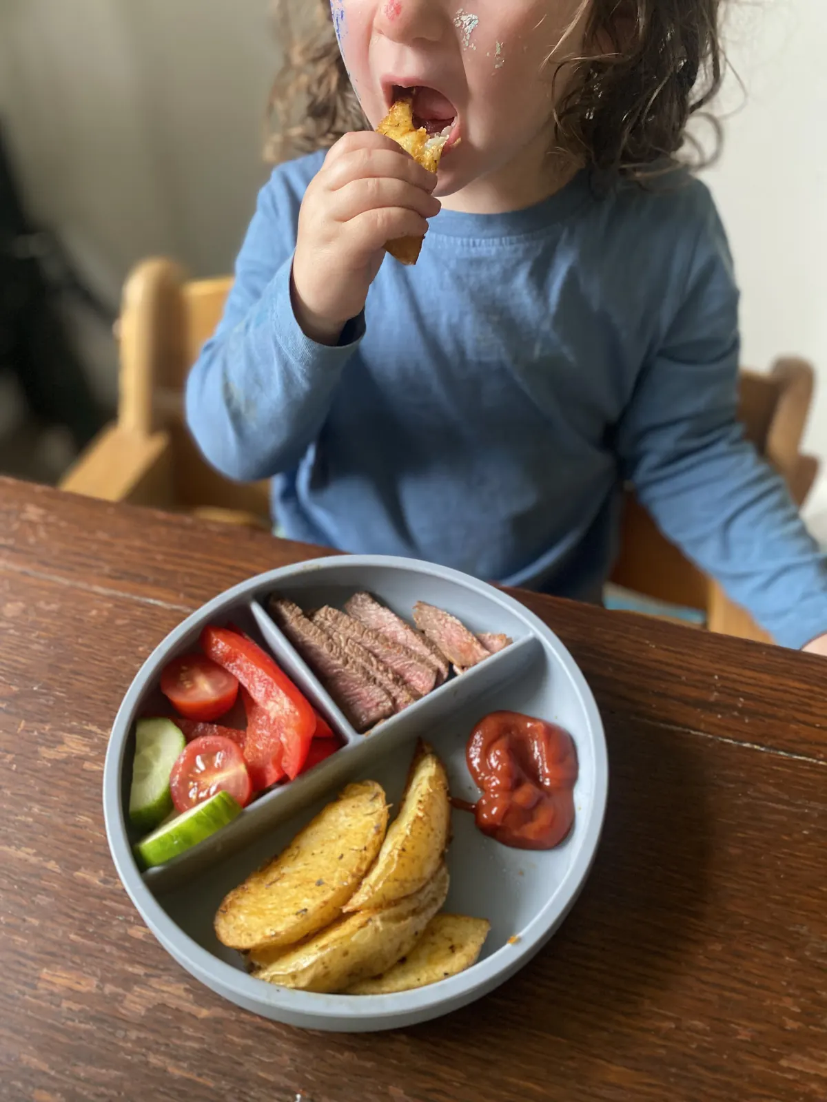 An older toddler eating from a blue divided plate.