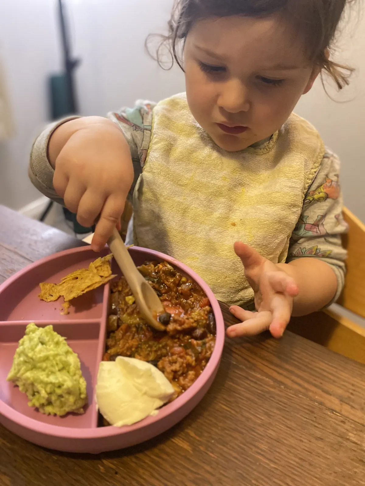 A child using a spoon against the divider of a pink plate.