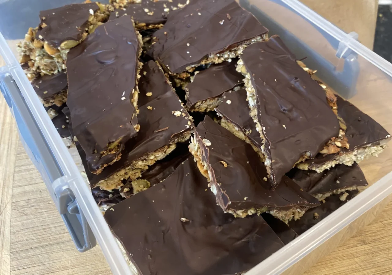 Pieces of homemade seedy chocolate bark stacked in a clear container.