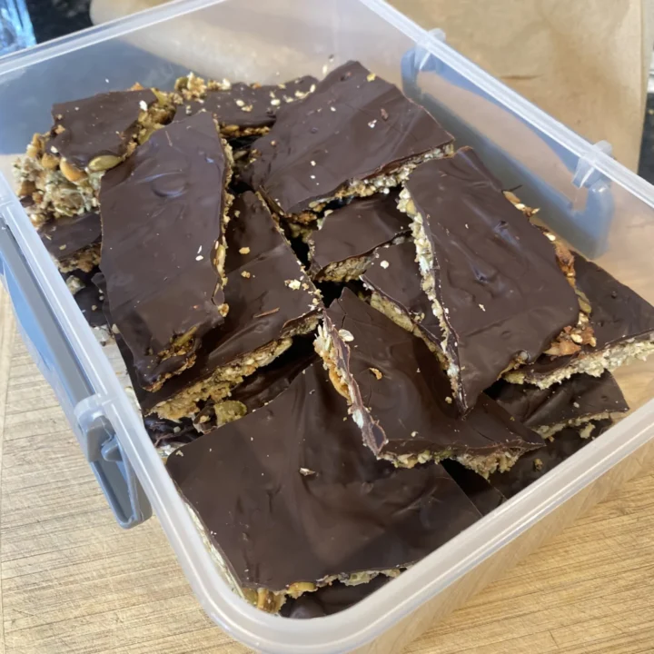 Pieces of homemade seedy chocolate bark stacked in a clear container.