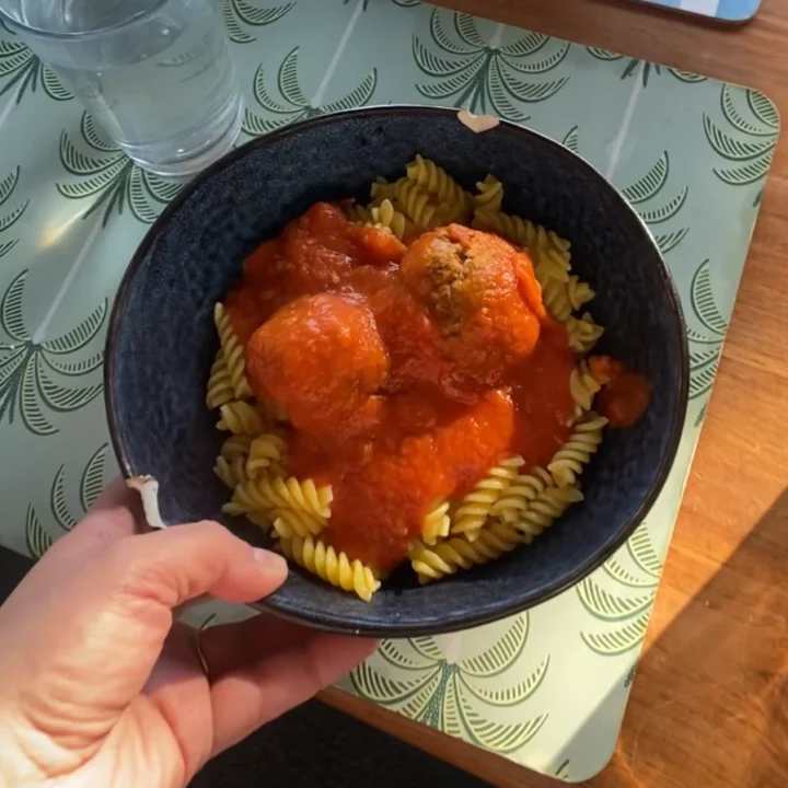 Pasta topped with tomato sauce and homemade meatballs in a dark bowl on a dining table.