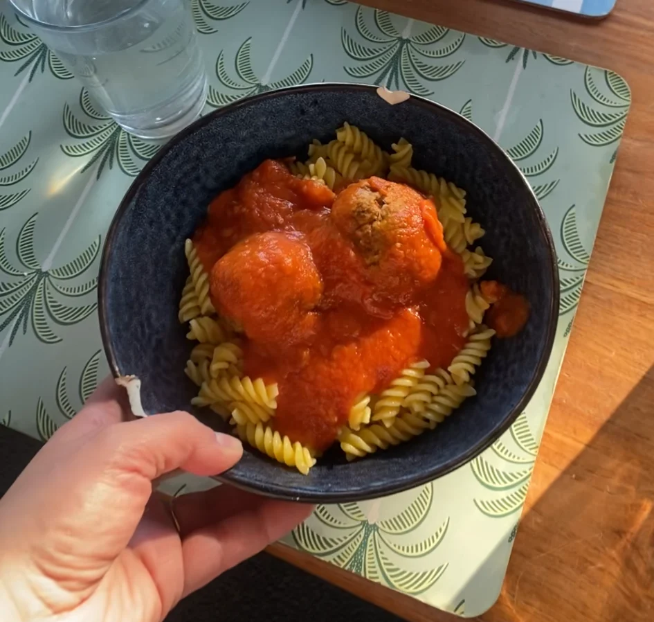 Pasta topped with tomato sauce and homemade meatballs in a dark bowl on a dining table.