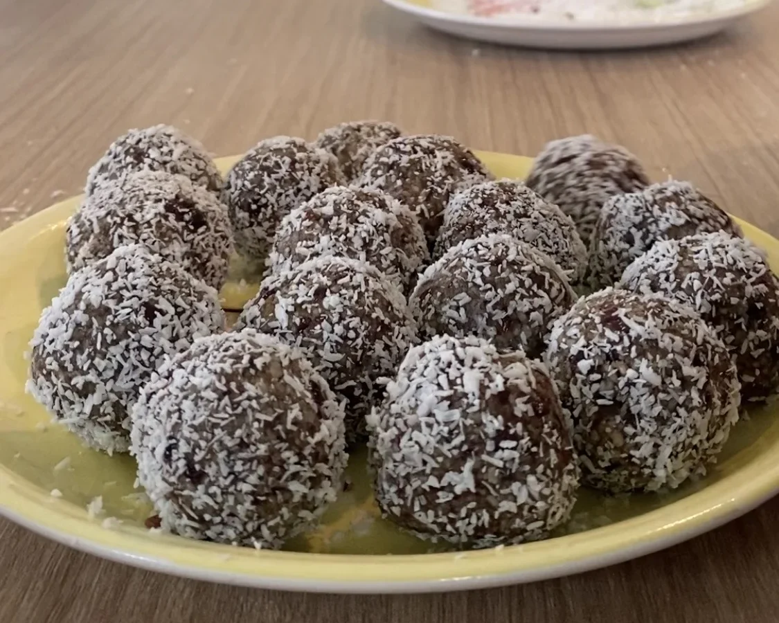 Coconut-coated raw balls on a yellow plate on a kitchen table.