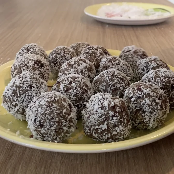 Coconut-coated raw balls on a yellow plate on a kitchen table.