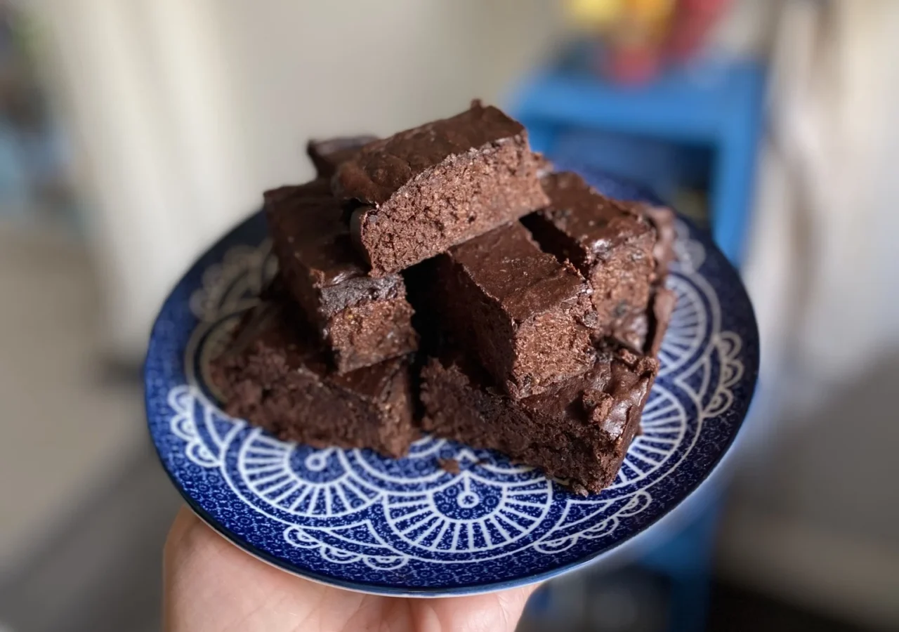 Stack of homemade chocolate brownies on a blue patterned plate held in one hand.