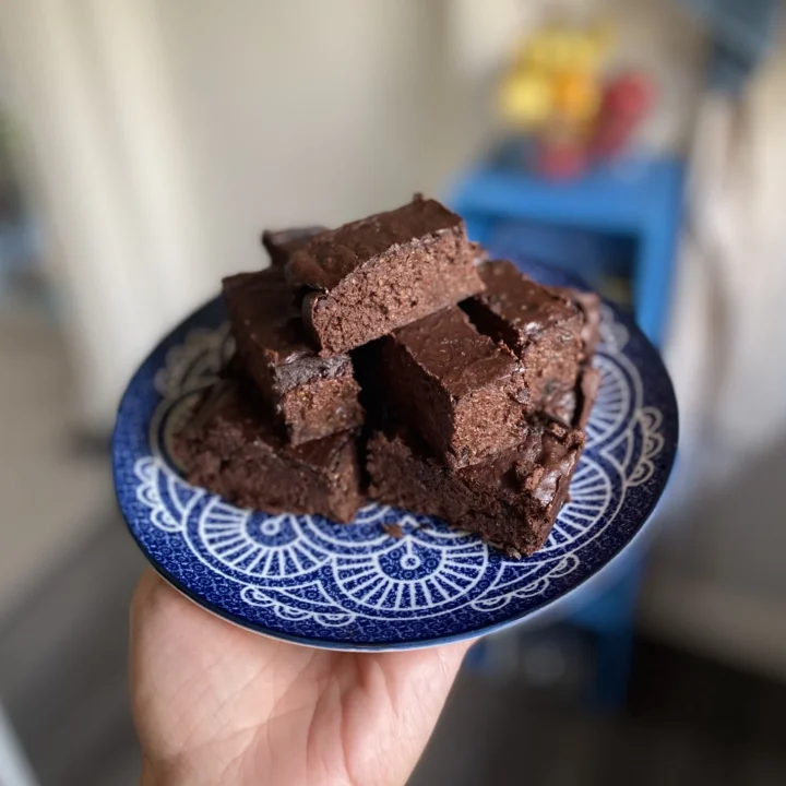 Stack of homemade chocolate brownies on a blue patterned plate held in one hand.